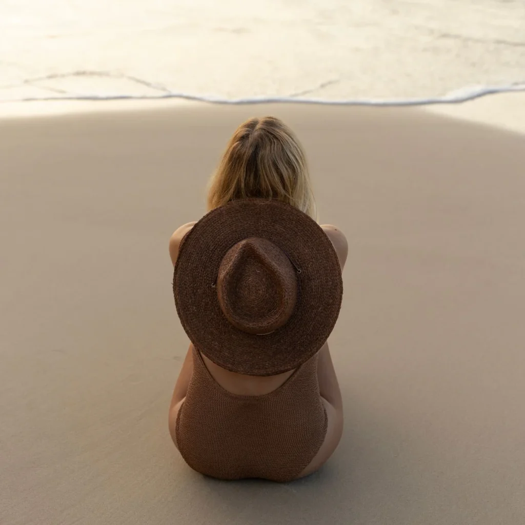 woman sitting on the beach with a Will & Bear hat on 